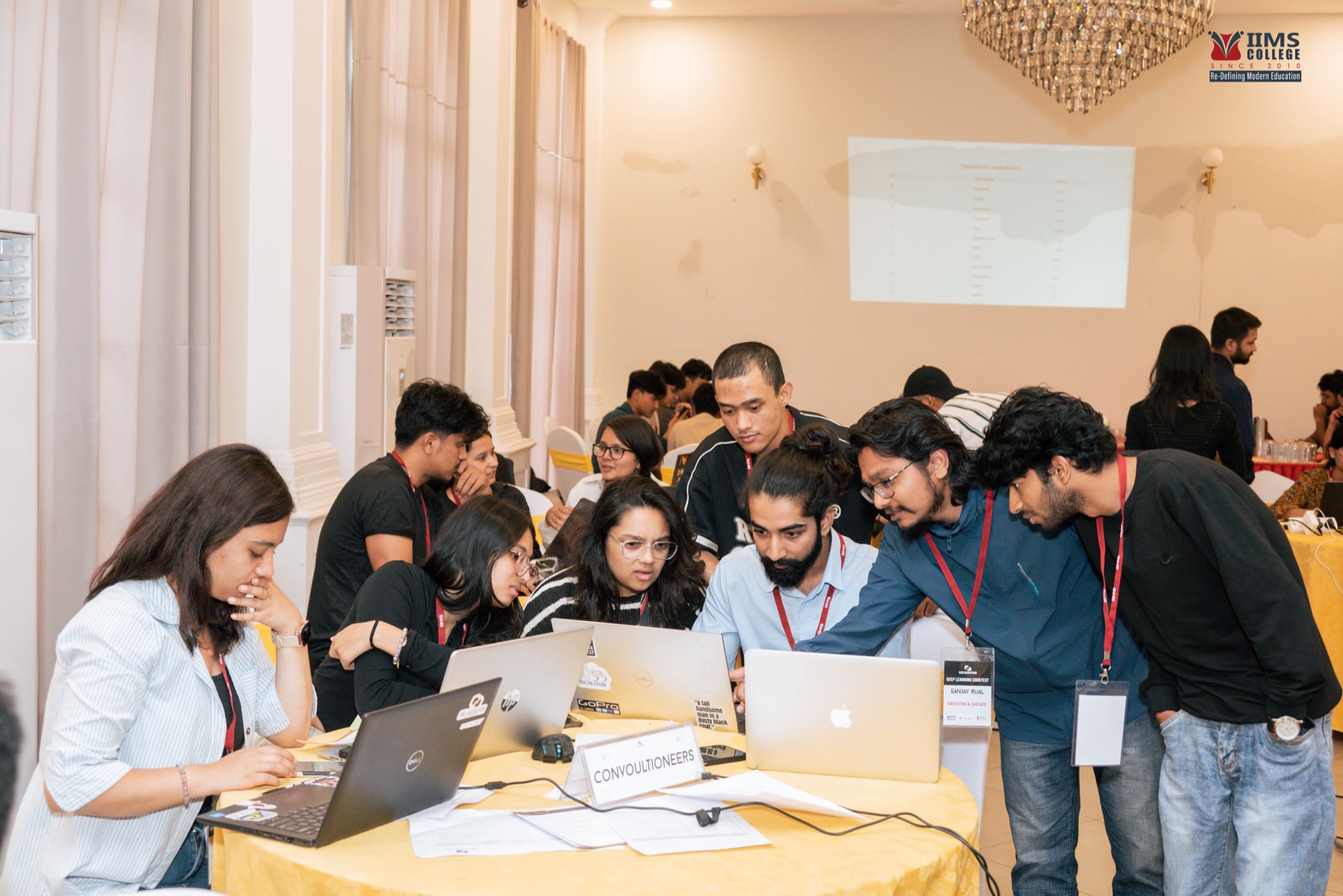 A student team and mentor reviewing work on several laptops